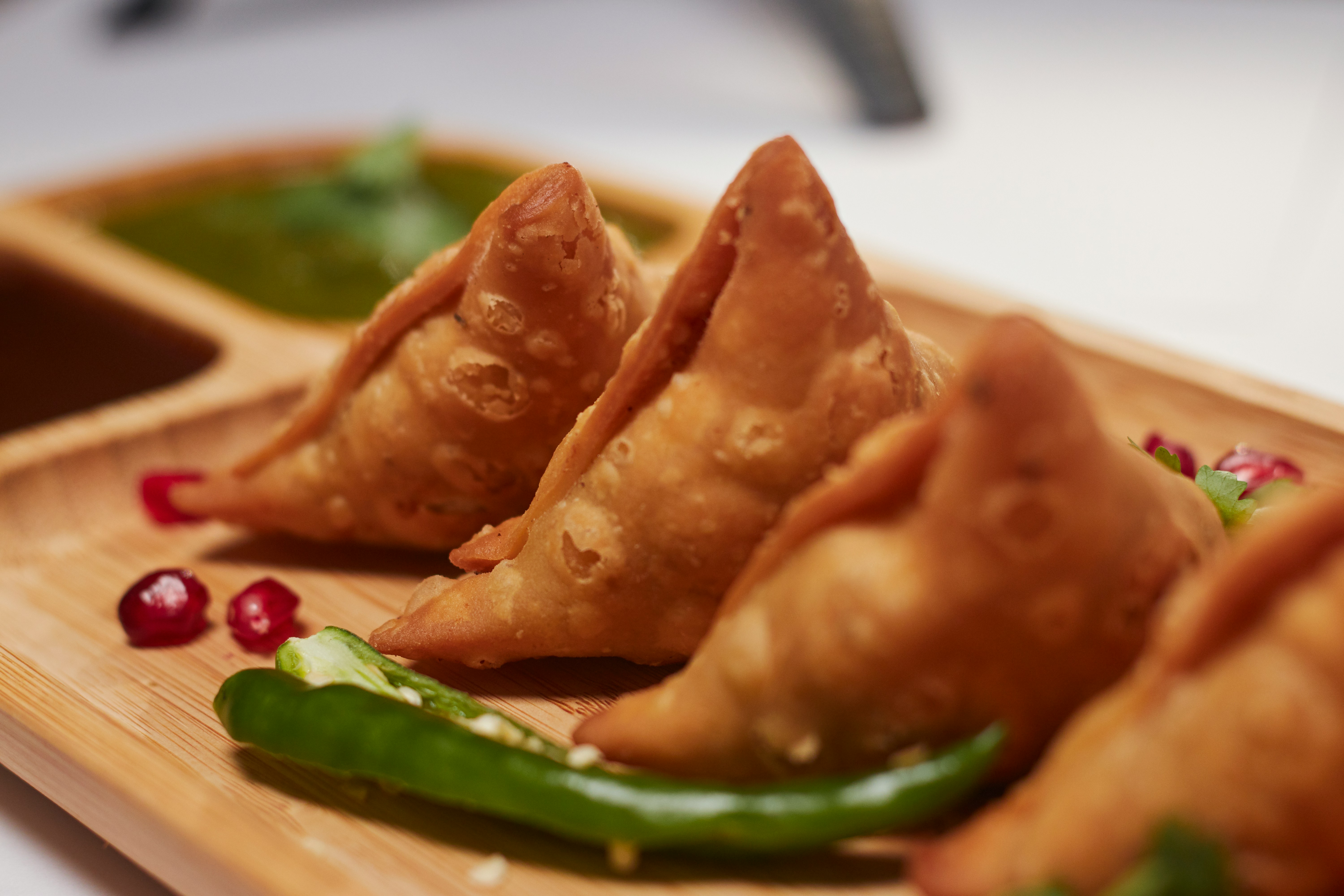 Picture of a plate of samosa with a chilli on the side and some garnish